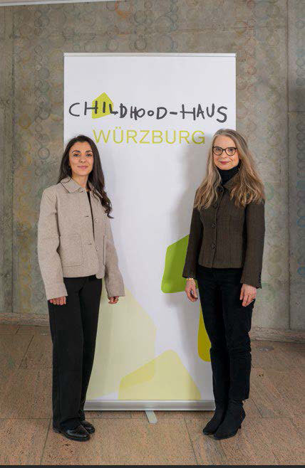 Maria Schuppan und Åsa Petersson vor dem Logo des Childhood-Hauses Würzburg.
